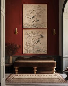 two paintings hang on the wall above a bench in a room with red walls and white trim