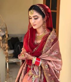 a woman in a red and gold bridal outfit is looking down at her hand