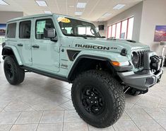 a light blue jeep is parked in a showroom with large tires on the front