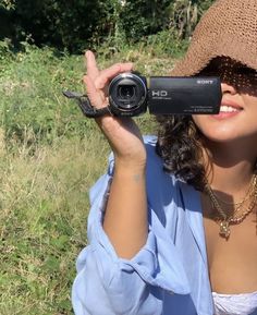 a woman wearing a hat and holding up a camera to take a photo in the grass