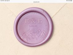 a purple wax seal with the initials r & b and mountains engraved on it's side