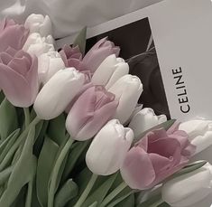 a bouquet of pink and white tulips sitting on top of a table next to a book