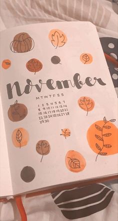 an open notebook with the word november written in black and orange on it, surrounded by fall leaves