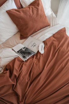 an unmade bed with two pillows and a book on the pillowcase next to it