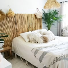 a bed with white linens and pillows in a bedroom next to a plant on the wall