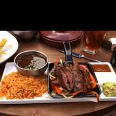 a plate with meat, rice and salsa on it next to a bowl of sauce