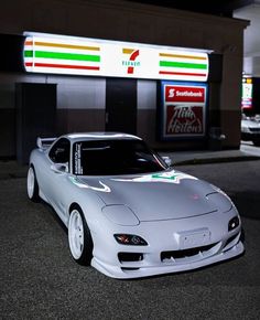 a silver sports car parked in front of a gas station at night with lights on