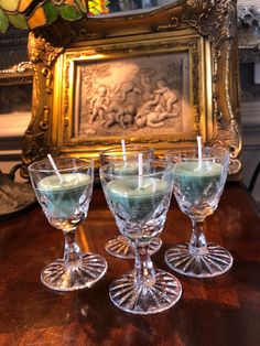 three glasses with candles in them sitting on a table next to a painting and ornate gold frame