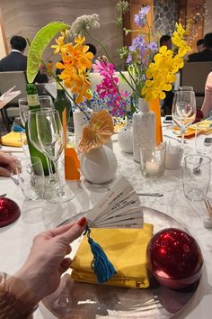 a person is sitting at a table with flowers in vases and napkins on it