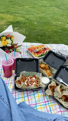 a picnic table with food and drinks on it in front of a grassy lawn area