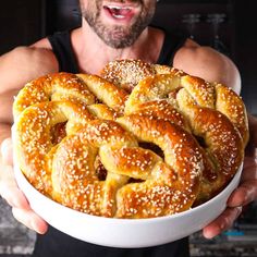 a man holding a large white bowl filled with pretzel breads in it's hands