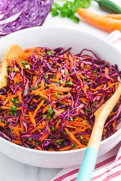 a white bowl filled with red cabbage and carrots next to some green onions on a table