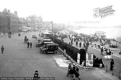 an old black and white photo of people walking on the street in front of cars