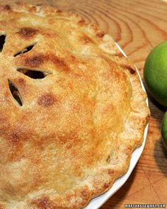 an apple pie sitting on top of a white plate next to two green pears