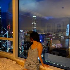 a woman sitting on top of a bed in front of a window overlooking a city