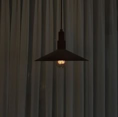 a light hanging from a ceiling in front of curtained windows with curtains behind it