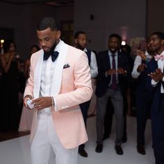 a man in a pink suit and bow tie is looking at his cell phone while others dance