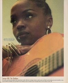 a woman holding an acoustic guitar in her right hand and looking up at the camera