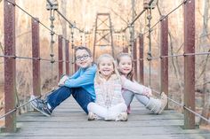 two young children sitting on a bridge in the woods with their arms around each other