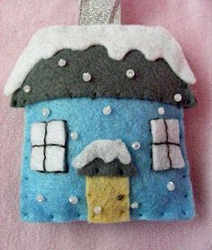 a felt house ornament hanging on a pink background