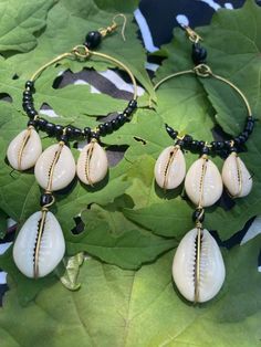 This cowrie shell is an important symbol that is steeped in a rich, ancient tradition in Africa. It symbolizes both spiritual connection to the ocean and goddess and material, earthly wealth. These Cowrie Shell Hoop Earrings contain the power of the cowrie shell in an elegant and regal pair of earrings. The large hoop earrings are brass with black beads. There are three polished white cowrie shells hanging from the earrings and an additional cowrie shell from the middle cowrie shell. Feel like a goddess in cowrie shell earrings today.  Made in Kenya. Gold Beaded Hoop Earrings For The Beach, Gold Bohemian Shell For Festival, Unique Adjustable Hoop Earrings For The Beach, Traditional Metal Jewelry For Beach, Shell-shaped Brass Jewelry For The Beach, Bohemian Handmade Shell Hoop Earrings, Handmade Shell Bohemian Hoop Earrings, Bohemian Metal Shell Jewelry, Bohemian Nickel-free Hoop Earrings For Beach