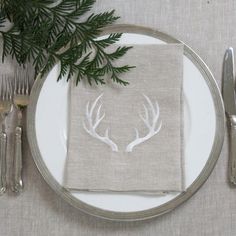 a place setting with silverware and napkins on a white table cloth decorated with deer antlers