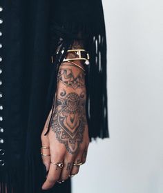 a woman's hand with tattoos on it and gold bracelets around her wrist