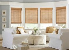 a living room filled with white furniture and windows covered in shades of brown blinds on top of them