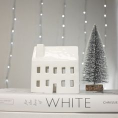 a white house sitting on top of a stack of books next to a christmas tree