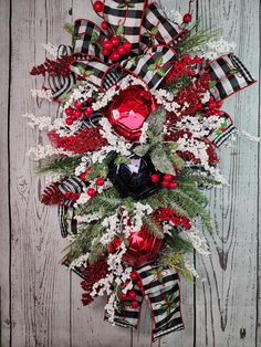 a christmas wreath with red and white flowers on a wooden background, decorated with ribbon