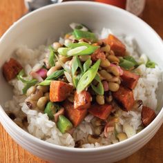 a white bowl filled with rice and vegetables on top of a wooden table next to a bottle