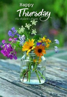 a vase filled with flowers sitting on top of a wooden table under a happy thursday sign