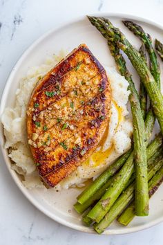 a white plate topped with meat and mashed potatoes next to green asparagus