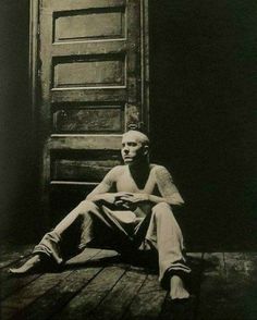 black and white photograph of a man sitting on the floor in front of a door