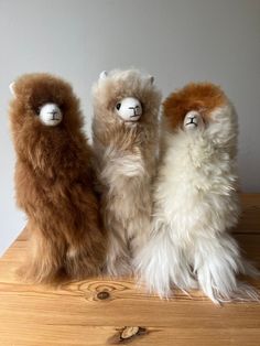 three stuffed llamas sitting on top of a wooden table next to each other