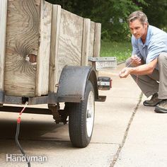 a man kneeling down next to a wooden box on the side of a road with a hose connected to it