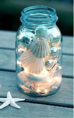 a mason jar filled with sea shells and christmas ornaments on a wooden table next to a starfish ornament