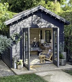 a backyard shed with patio furniture and potted plants on the outside, surrounded by greenery