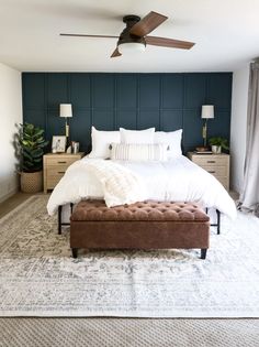 a bedroom with a bed, ottoman and ceiling fan