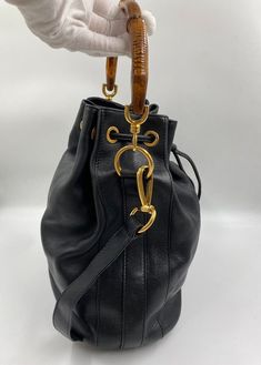 The cutest vintage black leather Gucci bucket bag with the iconic Gucci bamboo handles plus a leather crossbody strap. The crossbody strap can be taken off if you wish. This bag features gold Gucci branded hardware and gold feet on the base to protect the bag. Inside the lining is in excellent condition with a zipped interior pocket for valuables. The crossbody strap drop is 40cm. Gucci first introduced the bamboo handle in 1947 following a leather shortage as a result of the war, forcing crafts Gucci Bucket Bag, Black Bucket Bag, Gucci Brand, Black Bucket, Gucci Bamboo, Bag Inside, Bamboo Handles, Gucci Black, Diaper Backpack