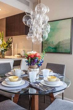 a glass table with plates and cups on it in front of a vase filled with flowers