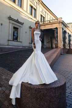 a woman in a white wedding dress standing on a brick walkway near a large building