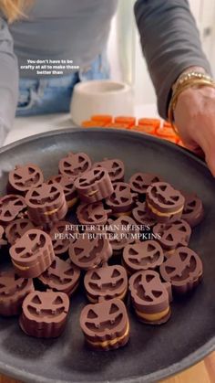 a woman holding a pan filled with chocolate covered pretzel cookies on top of a counter