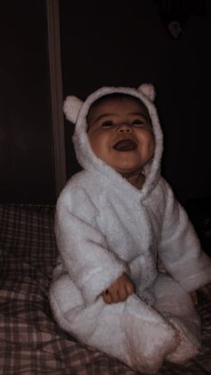 a baby in a bear costume sitting on top of a bed wearing a white robe