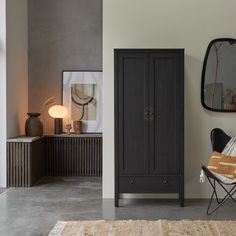 a black cabinet sitting next to a chair in a room with a mirror on the wall