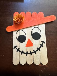 popsicle stick scarecrow with orange hat on wooden table next to paper plate pumpkin