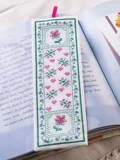 an open book with a cross - stitch pattern on it and a pink string attached to the cover