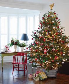 a decorated christmas tree sitting in the corner of a living room next to a red chair