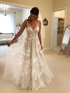 a woman wearing a wedding dress with flowers on the skirt and veil, standing in a room