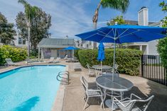 an outdoor pool with chairs and umbrellas next to a fenced in backyard area